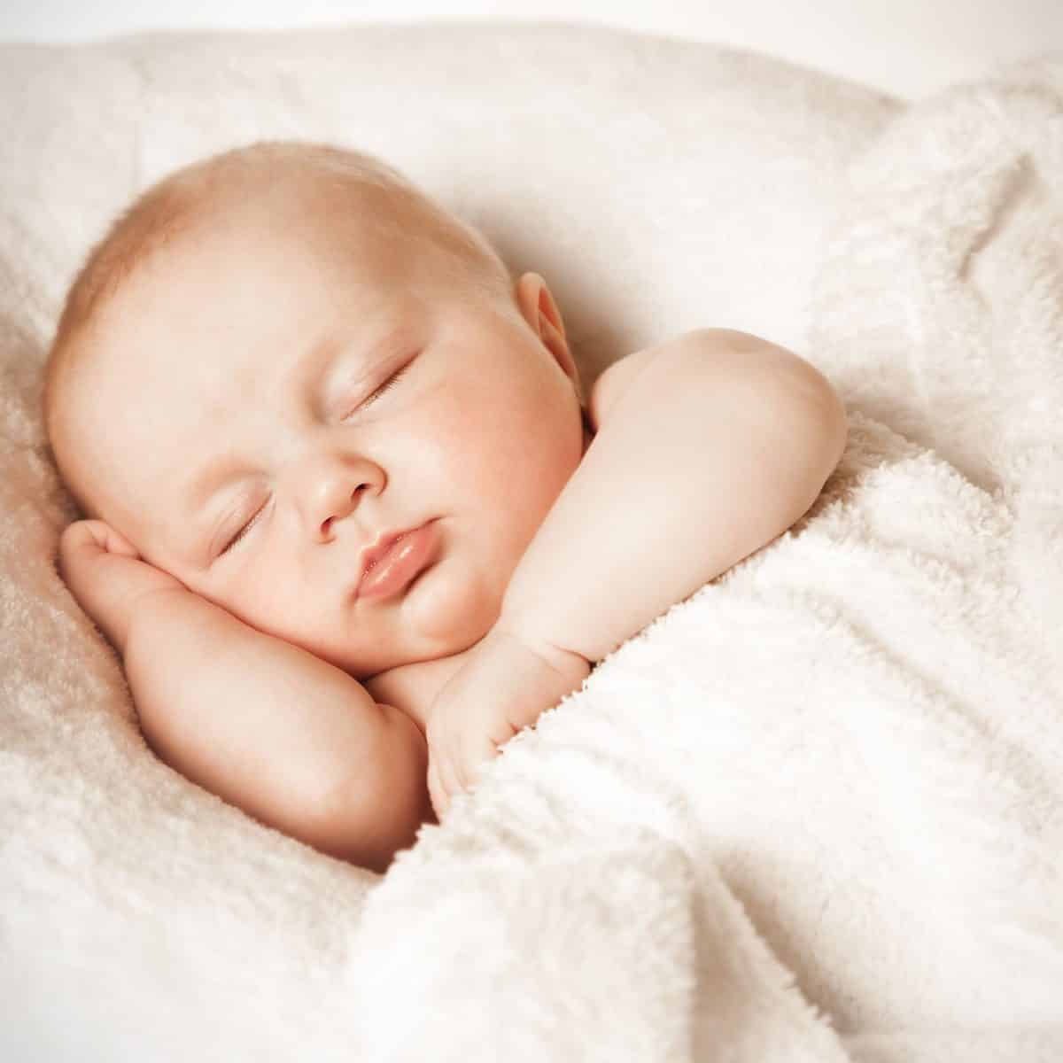 A baby sleeping comfortably with its head resting on one hand and the other across its chest