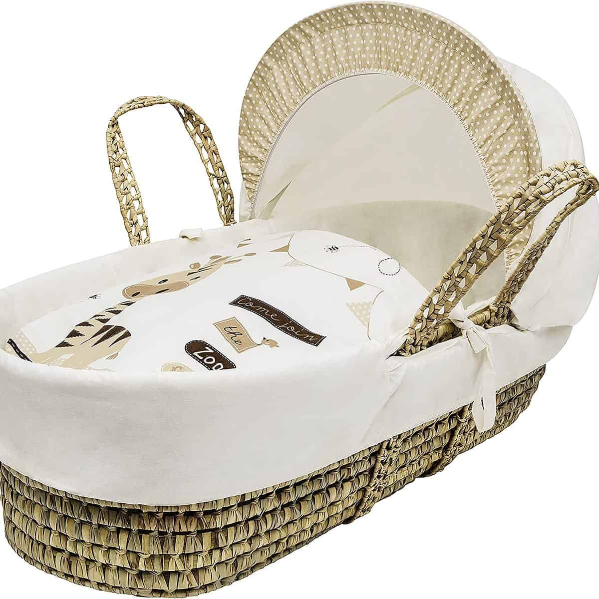 A Moses basket with hood and white linens with a zoo pattern