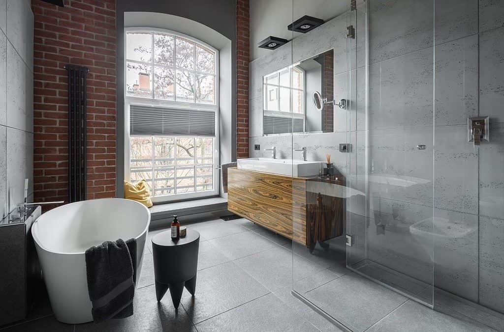 An industrial styled bathroom in grey stone and brick with circular tub and walk in shower