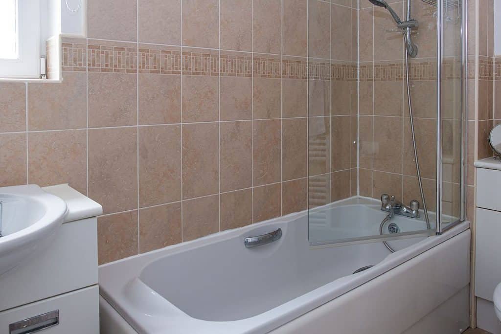 White bath with pastel tiles and a shower with shower screen