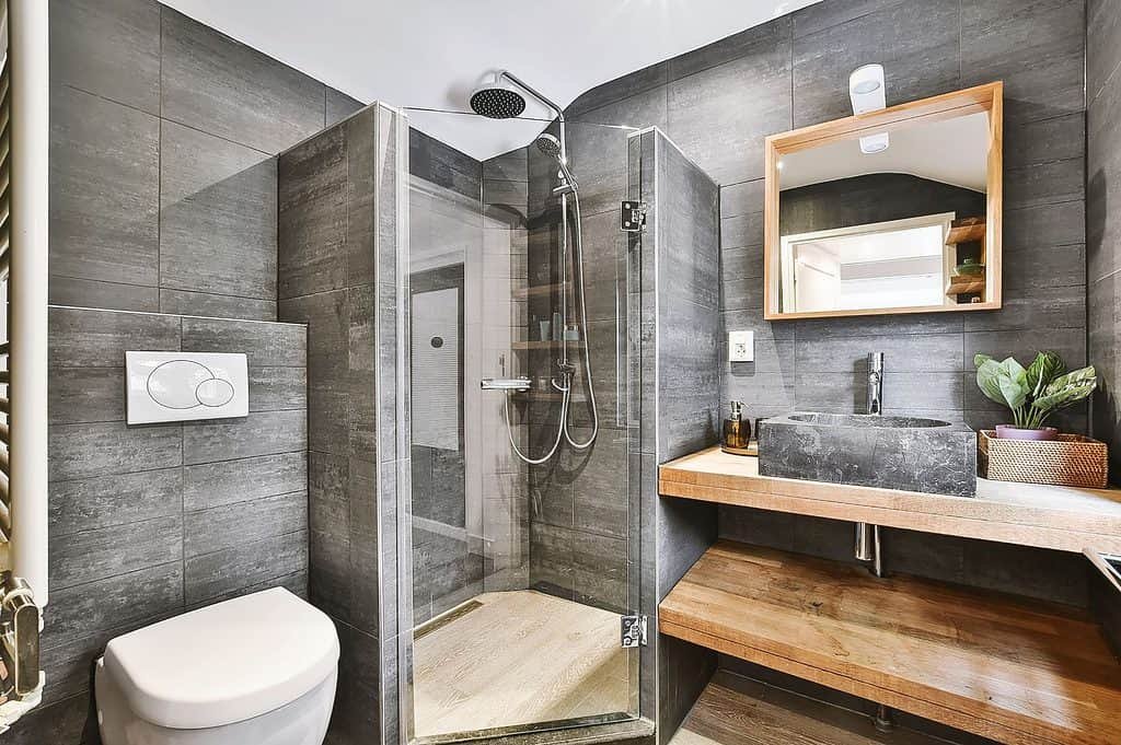 A modern grey bathroom with a toilet on the left, a corner shower in the centre and a basin on the right