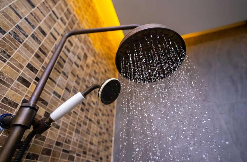 A large rain fall shower head with water coming out plus a handheld shower head