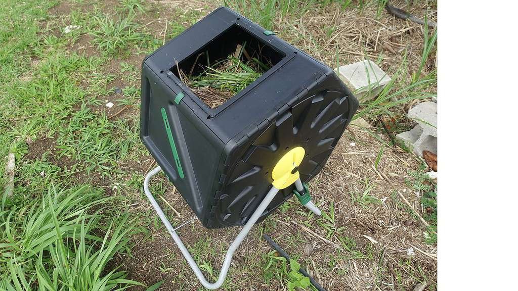 A small black compost tumbler with its lid open showing some garden waste