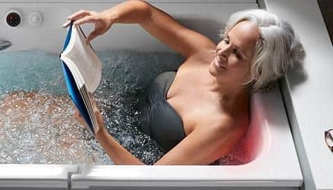 a photo of a woman comfortably bathing in a walk in bath while reading a book
