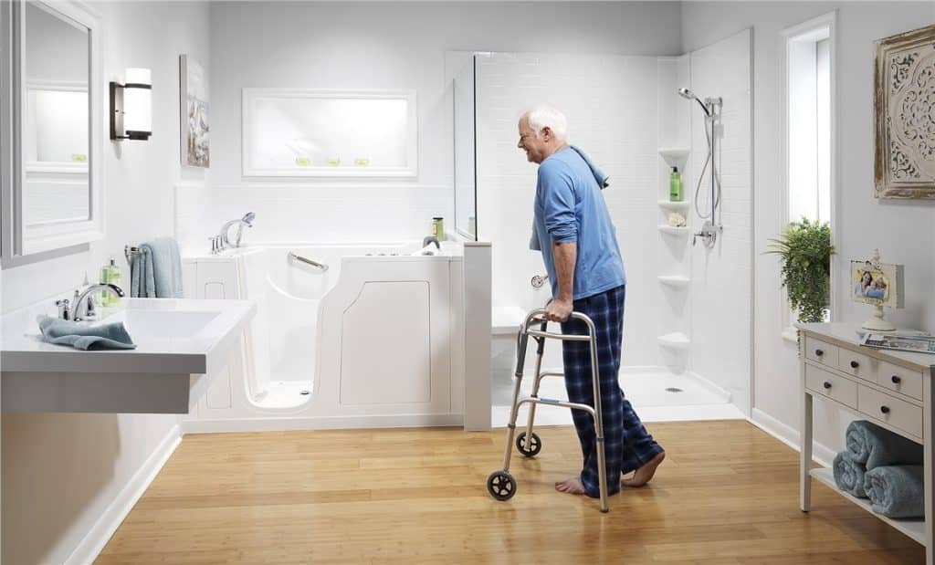 An image of an elderly man using a steel walker as he walks towards a walk-in bath